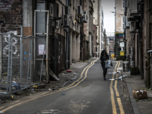 a woman carries shopping down a run-down street
