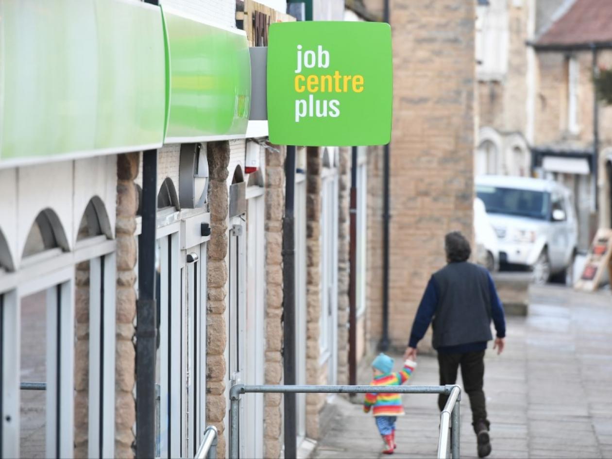 an adult holding a child's hand as they walk down a pavement outside a job centre plus