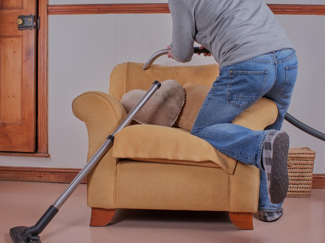 a man kneels on an armchair as he hoovers the upholstery