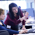 two women are in front of a computer. One
