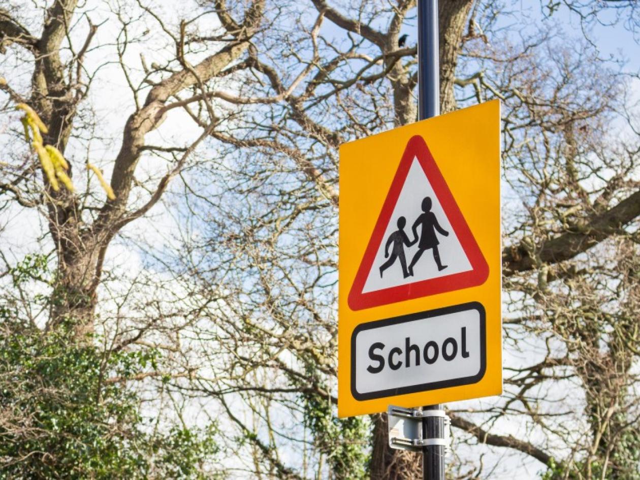 a school roadsign showing silhouettes of children crossing a road in a red triangle