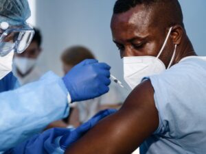 a man wearing a face mask receives an injection from someone wearing protective equipment