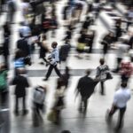 A group of people moving across a station concourse in different directions, blurring as they move