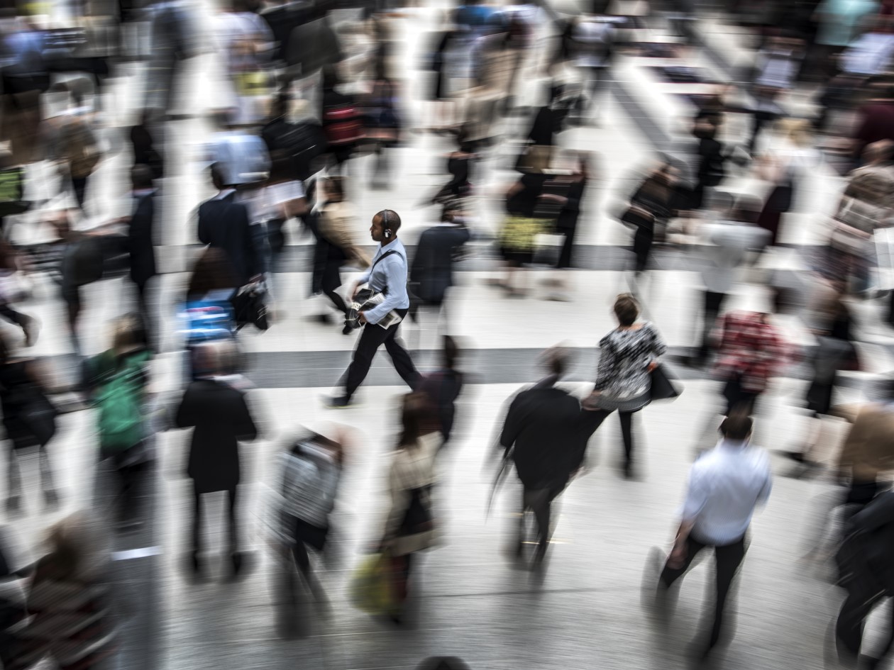 A group of people moving across a station concourse in different directions, blurring as they move