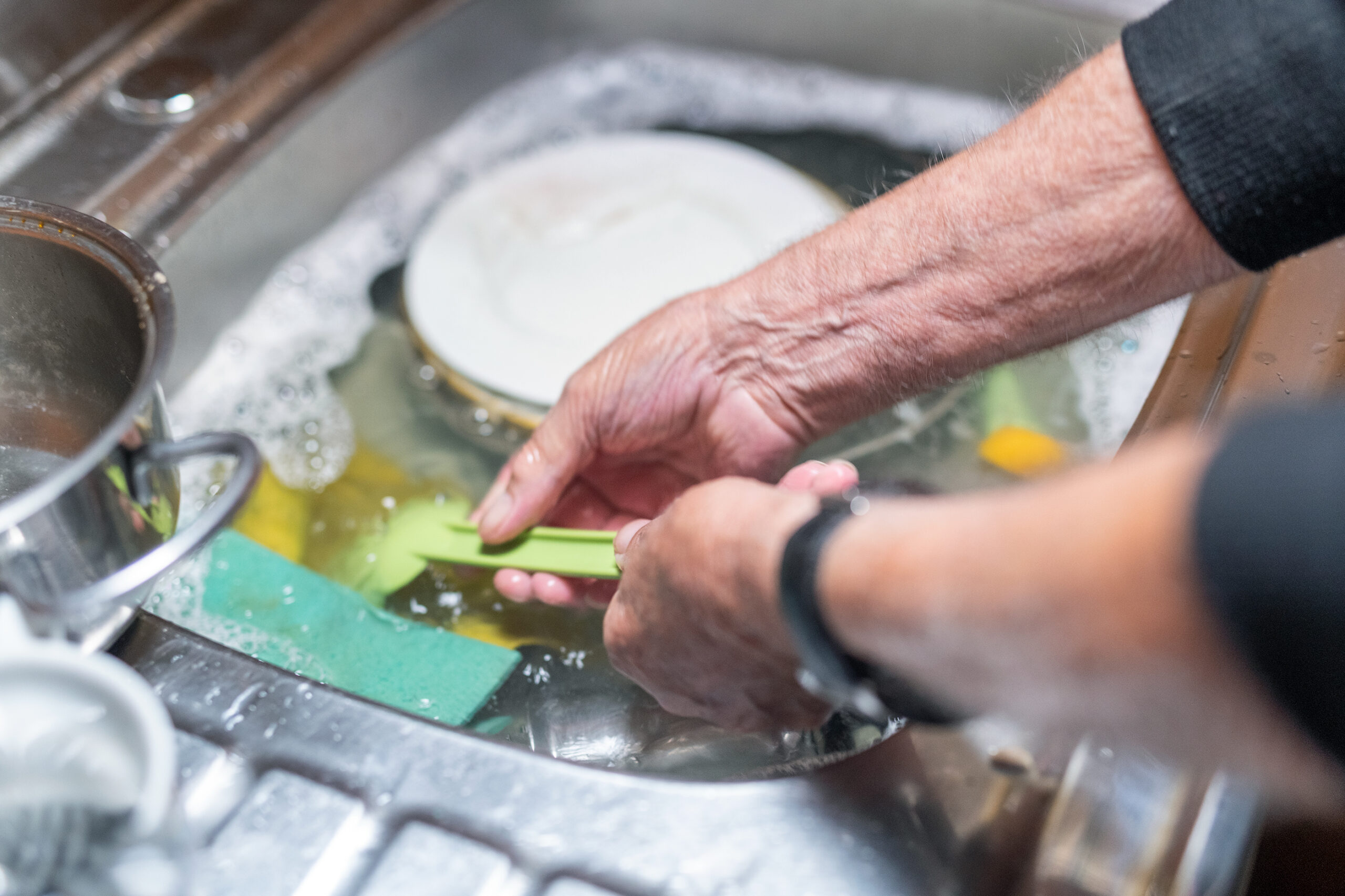a man washing up in a sink. The photo focuses on his hands and forearms